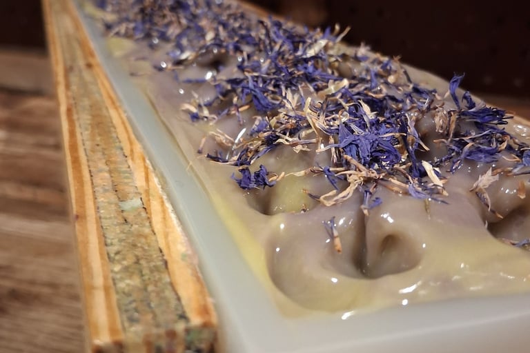 Handmade huckleberry soap loaf in a wooden mold topped with dried blue cornflower petals.