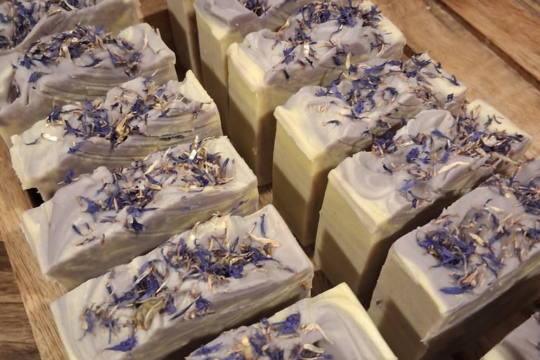Handmade artisanal lavender soap bars topped with dried blue cornflowers on a wooden drying rack.