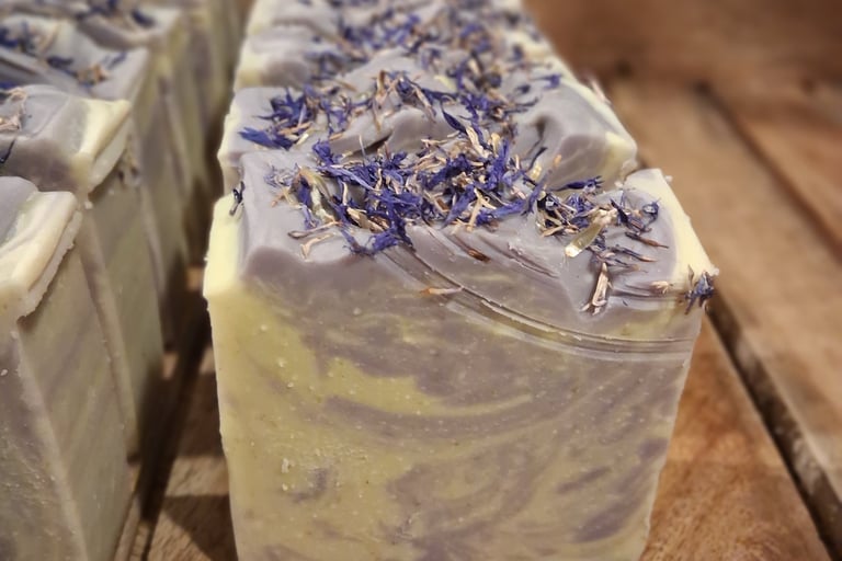 Handmade huckleberry artisan soap bars with dried botanical petals on a rustic wooden tray.