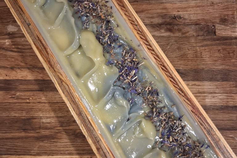 Handmade Blue soap loaf in a wooden mold topped with dried botanical flower buds on a rustic table.