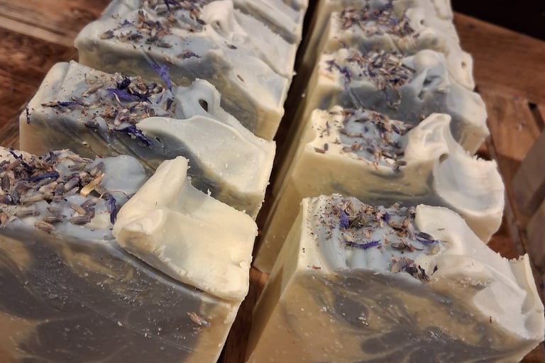 Handmade soap bars with swirls of grey and white topped with dried botanical flowers on a wooden tray.