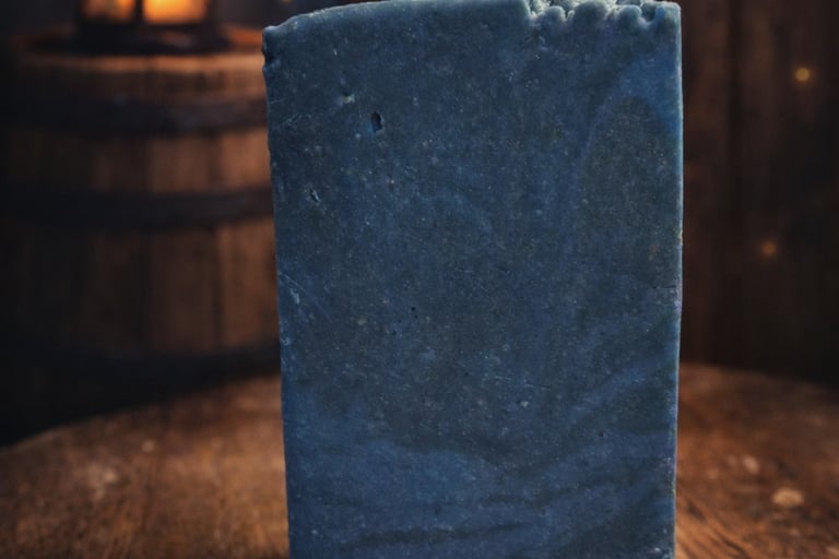 Handmade rustic blue bar soap on a wooden table with a lantern background.