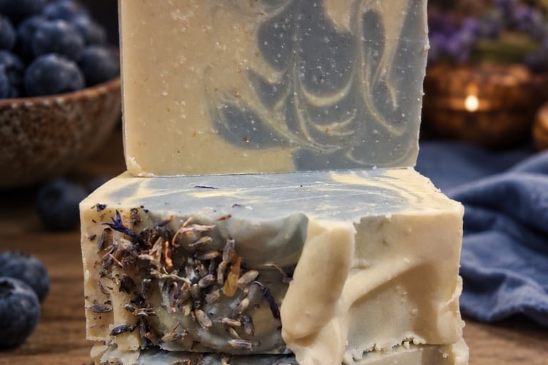 Handmade blueberry soap bars stacked on a rustic wood table with fresh berries.