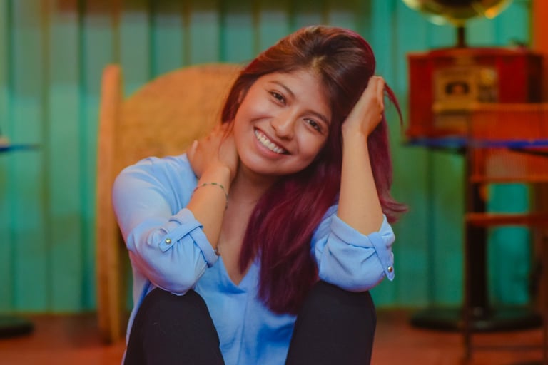 A smiling young woman with auburn hair wearing a blue blouse posing indoors.