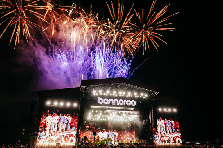 Fireworks explode over the Bonnaroo music festival main stage at night during a live concert performance.
