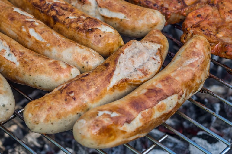 Juicy bratwurst sausages with grill marks cooking on a charcoal barbecue grill.