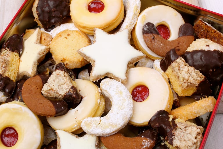 Assorted Christmas cookies including jam-filled linzer, chocolate crescents, and iced stars in a tin.