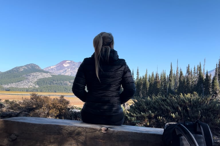 Anneke, zittend op een bankje, uitkijkend over bomen en een berg - het gevoel van vertragen