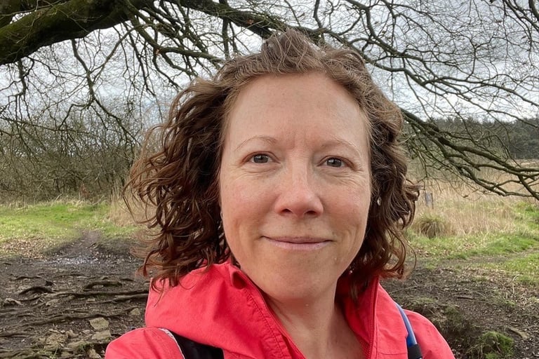 photo of Iona Reading, Health Coach in red jacket standing in front of a tree smiling