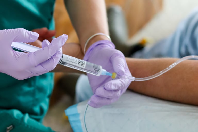 Nurse in green scrubs and purple gloves administering IV therapy blend through a patient's IV line.