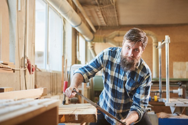 man with check shirt using a drawknife on timber
