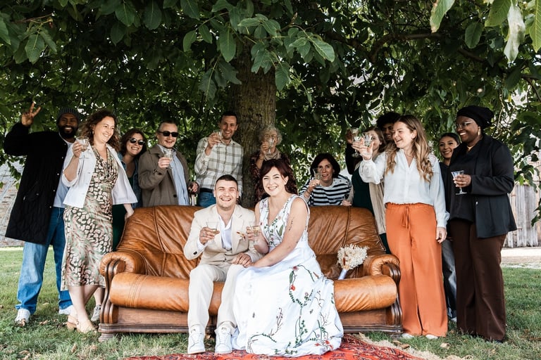 Un couple de mariés sur un canapés entourés de leurs invités