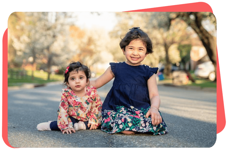 two young girls sitting on the ground in front of a tree