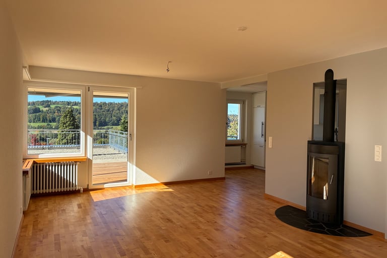 Spacious empty living room with hardwood floors, a modern black fireplace, and a balcony with a scenic mountain view.