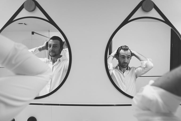 Artistic shot of two men fixing their hair, captured through a mirror reflection at a wedding venue