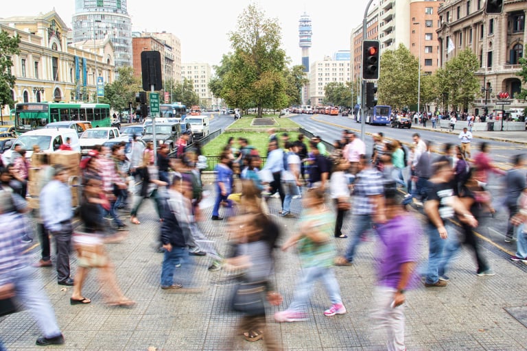 Pedestrians crossing a busy street. Cars, buses, other pedestrians, and buildings are visible in the background.