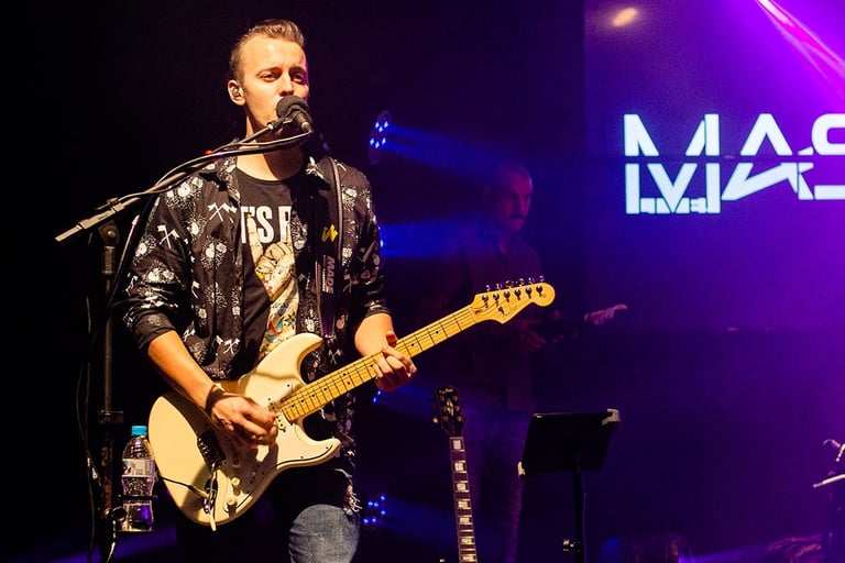 Guitarist and singer Lucas Vianna playing his white Fender Stratocaster guitar while singing.