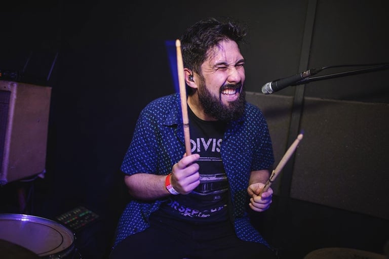 Drummer Lucas Dias playing the drums with his eyes closed, holding two drumsticks.