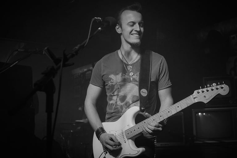Guitarist and singer Lucas Vianna playing his white Fender Stratocaster guitar with his eyes closed and smiling.
