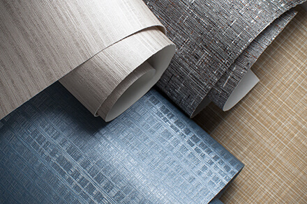 Close-up of textured wallpaper rolls in neutral tan, grey, and blue crosshatch patterns.