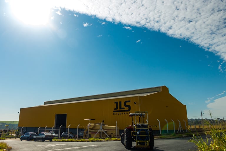 Pulverizador pecuário com a fábrica da JLS Máquinas ao fundo