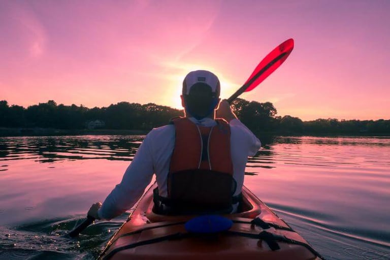 man paddling a kayak on a lake with the sun setting in the distance