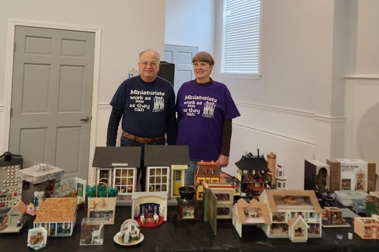 A picture of a man and woman with a table full of miniautre houses.