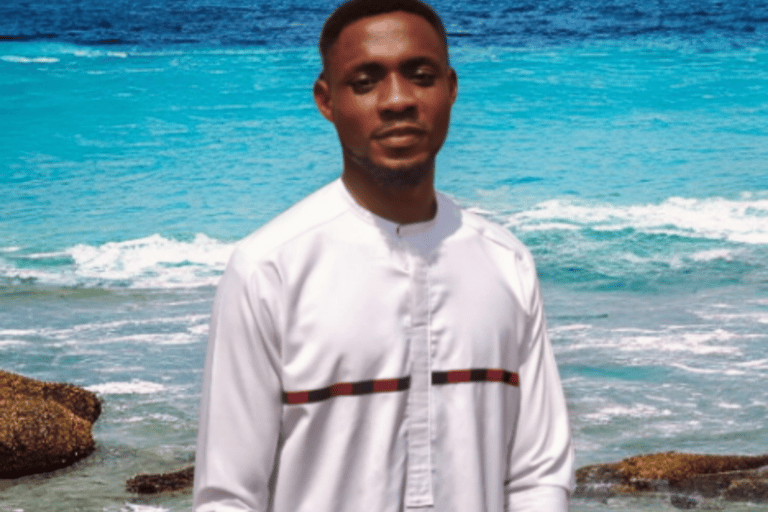 a man in a white shirt and jeans standing in front of a body of water