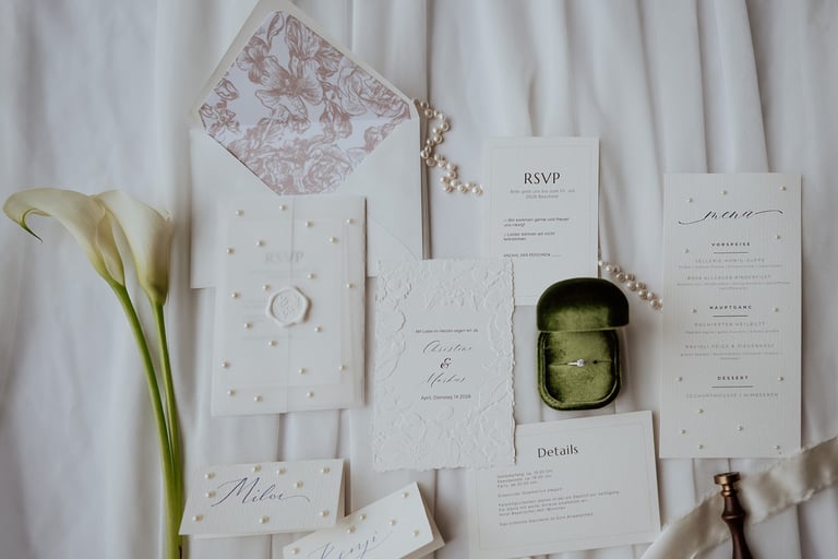 Elegant white wedding invitation suite with floral envelopes, pearl accents, and a green velvet ring box.