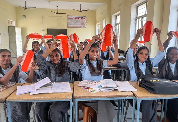 Class of young schoolgirls holding up a Hanaru reusable sanitary napkin in a schoolroom