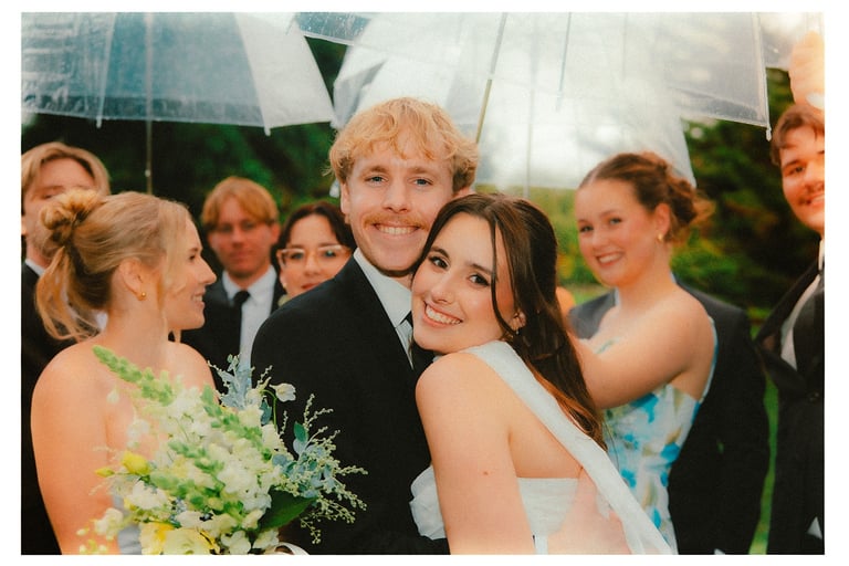 Bride and groom celebrating with their bridal party under clear umbrellas
