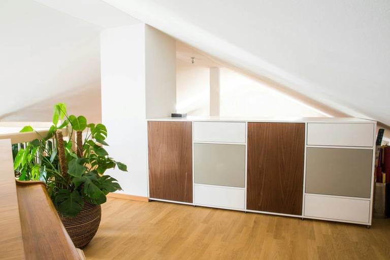 Mobilier blanc et bois foncé, mur blanc, parquet clair, plante verte dans pièce sous comble