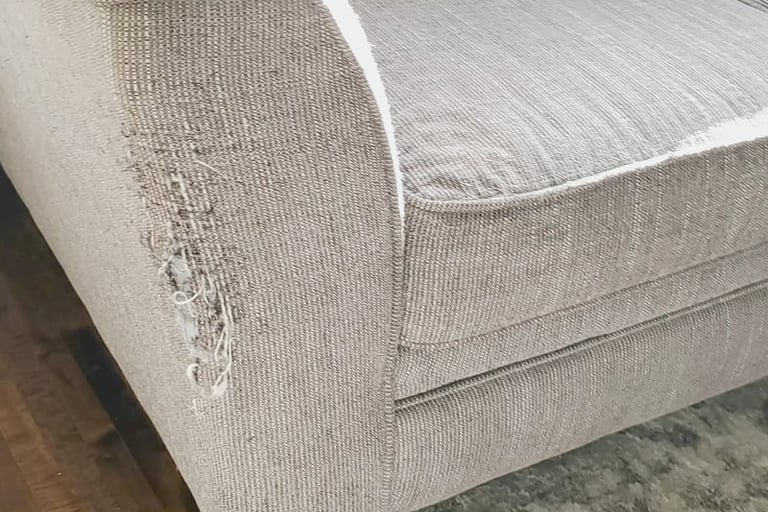 A close-up of a modern light gray textured fabric sofa with tapered wooden legs on a shag rug.