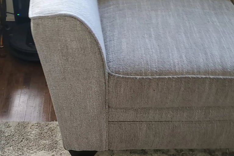 Close-up of a light gray textured fabric sofa on a plush area rug in a modern living room.