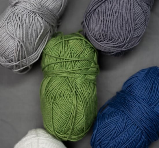 Colorful skeins of yarn in gray, green, blue, and white tones arranged on a neutral fabric backgroun