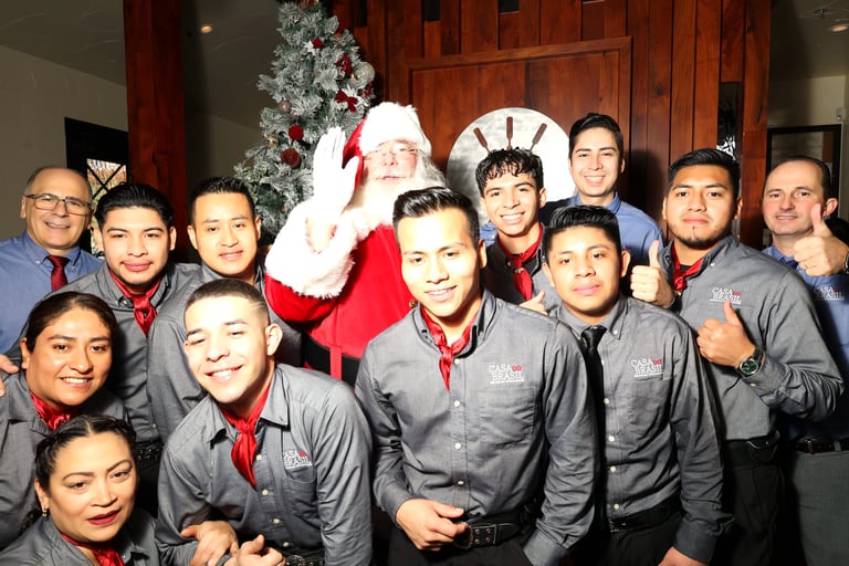 a group of people standing around a man dressed in a santa clause costumeat Casa Do Brazil