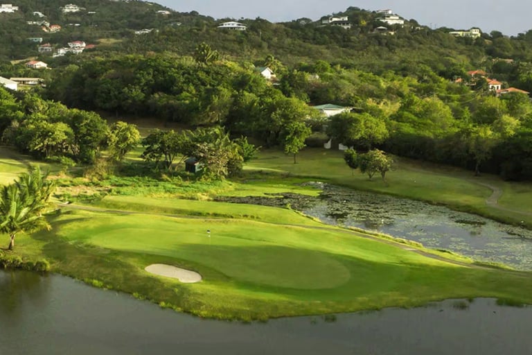 A lush tropical golf course green with water hazards, bunkers, and hillside villas in a Caribbean landscape.