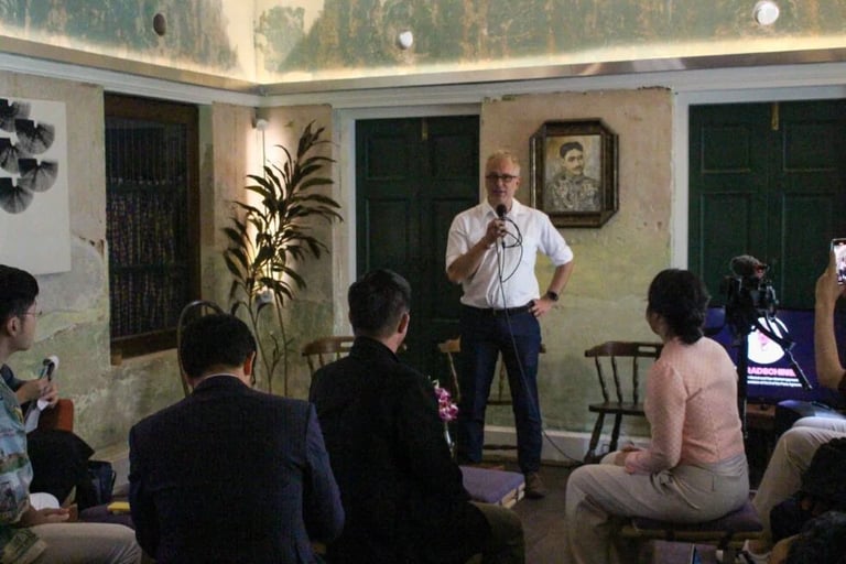 A man in a white shirt speaking into a microphone at a public talk event.