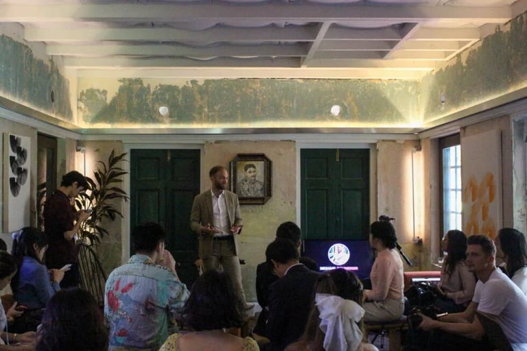 Speaker in a suit leading a business presentation and discussion for an audience in a rustic indoor venue.