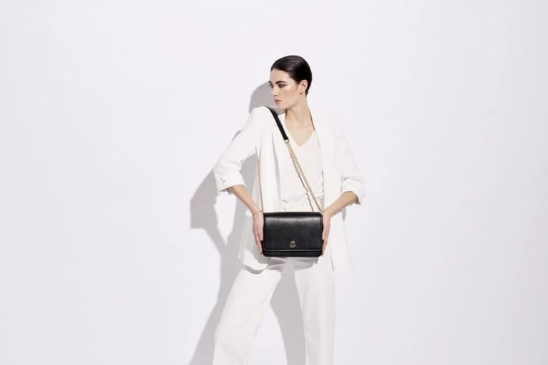 A woman in a white suit holding a black leather crossbody bag with a gold chain strap.