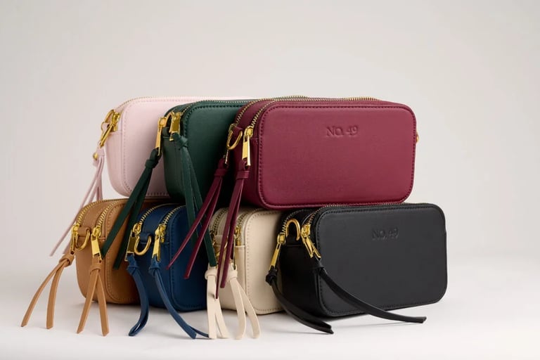 A stack of colorful vegan leather crossbody bags with gold zippers and tassel details for women's fashion.