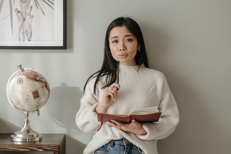 woman holding a pencil and red notebook, studying thoughtfully in a minimalist workspace.