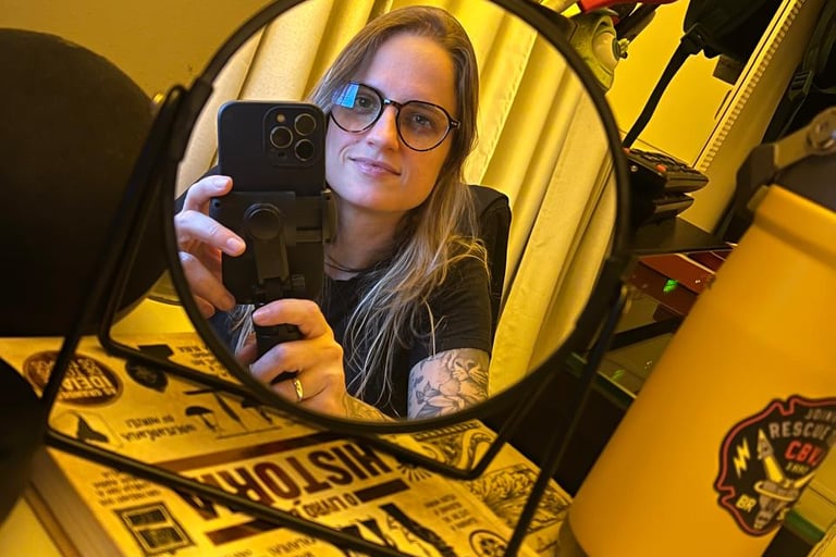 Woman with glasses taking a mirror selfie on a desk with books and office supplies.