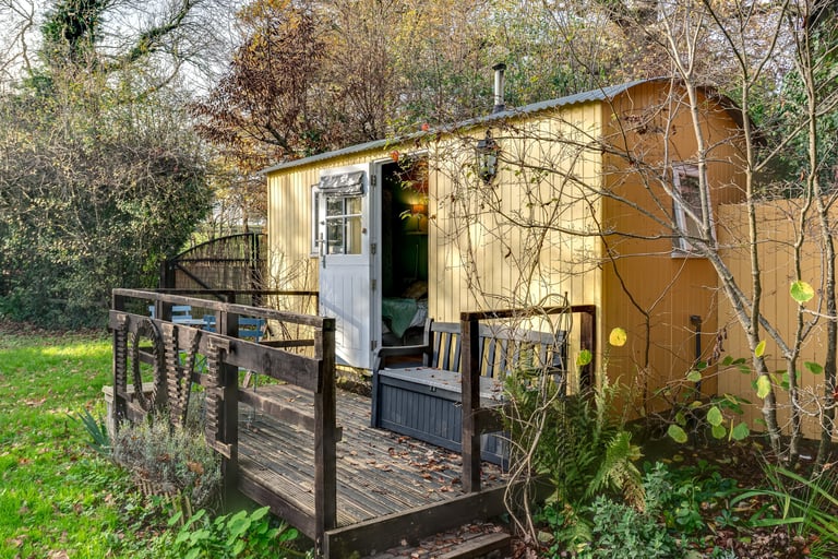A cozy yellow shepherd's hut with a wooden deck and 'LOVE' sign nestled in a garden.