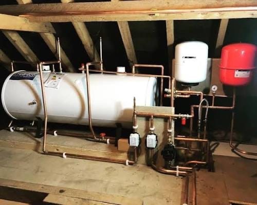 Unvented hot water cylinder with copper piping and expansion vessels installed in a residential loft space.