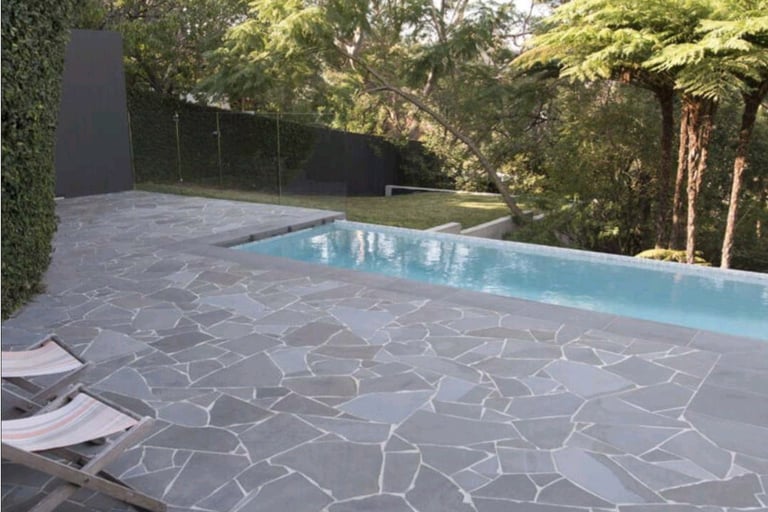 Crazy Paving - Stone patio with two lounge chairs beside a rectangular pool surrounded by lush trees