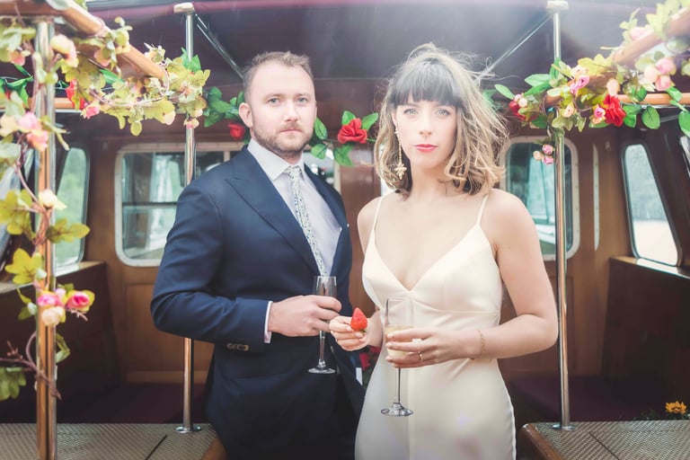 Elegant couple in wedding attire celebrating with champagne and strawberries on a decorated boat.