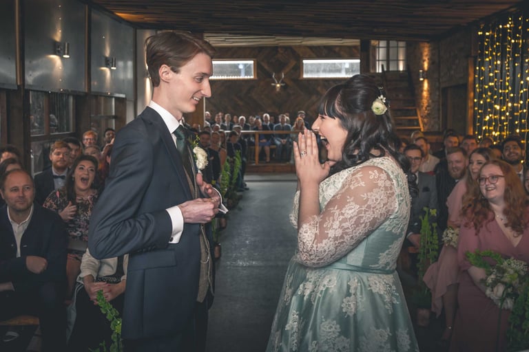 A groom and bride exchanging vows during an indoor rustic wedding ceremony at a barn venue.