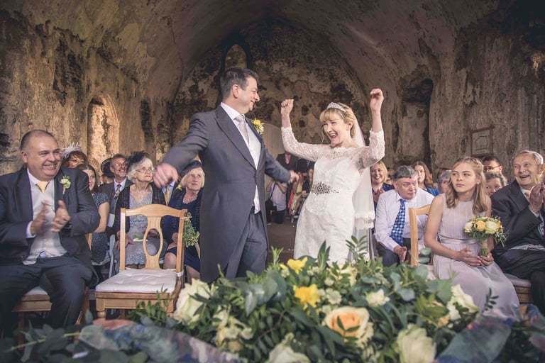 A joyful bride and groom celebrating their wedding ceremony inside a historic rustic chapel with guests.