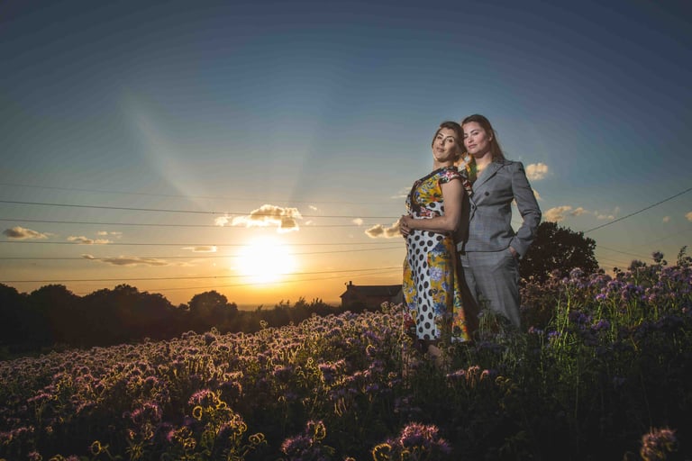A couple poses in a field of purple wildflowers during a golden hour sunset.